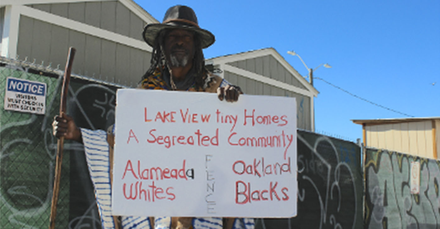 Nino Parker holds a sign outside of The Lakeview Village tiny homes on Feb. 22. Photo by Zack Haber.