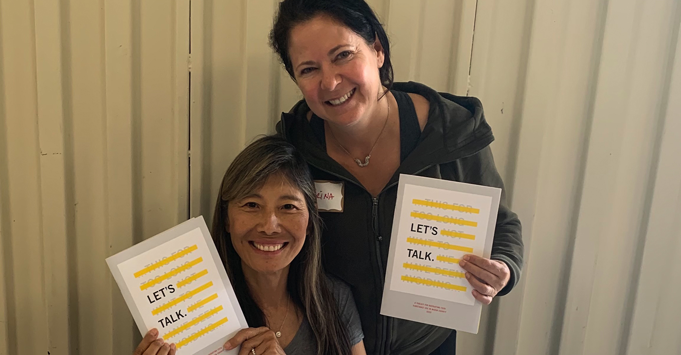 Two volunteers hold up the new “Let’s Talk” booklet at a recent distribution event.