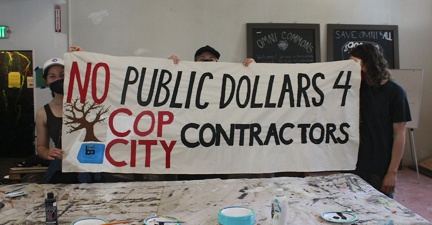 At an art creating event in the Omni Commons in Oakland, activists hold a banner calling for divesting Bay Area public funds from The Atlanta Public Safety Training Center, which is commonly known as “Cop City.” Photo by Zack Haber on June 3.