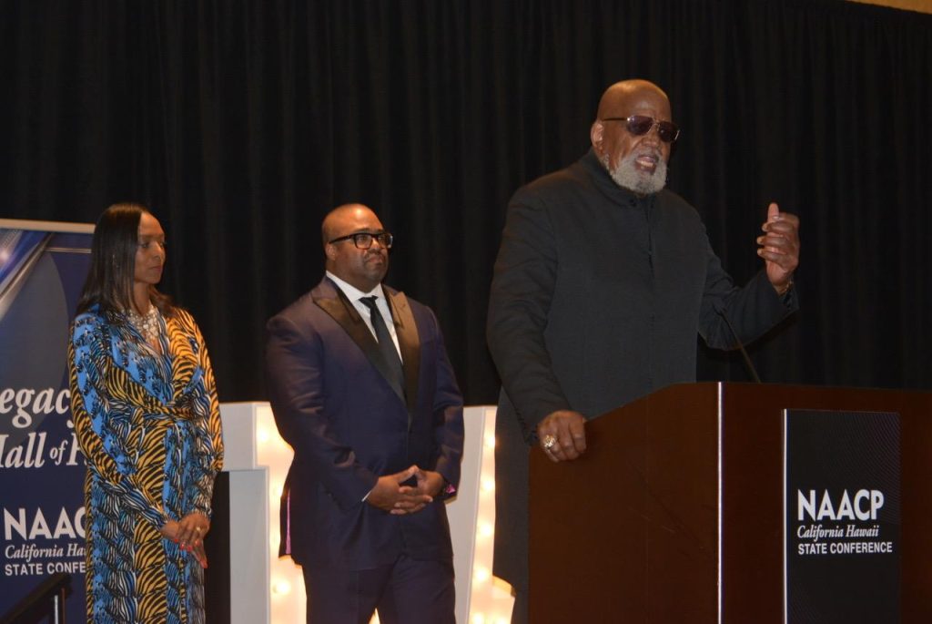 Dr. Harry Edwards (Legacy Hall of Fame recipient), at the podium, and Dr. Kenneth Noel organized the protest at the 1968 Olympics in Mexico City. He is shown here with CA/HI NAACP President Rick Callendar and Carolyn Veal-Hunter (CA/HI NAACP treasurer) at the Legacy Hall of Fame induction ceremony in Sacramento, June 24, 2023. CBM photo by Antonio Ray Harvey.