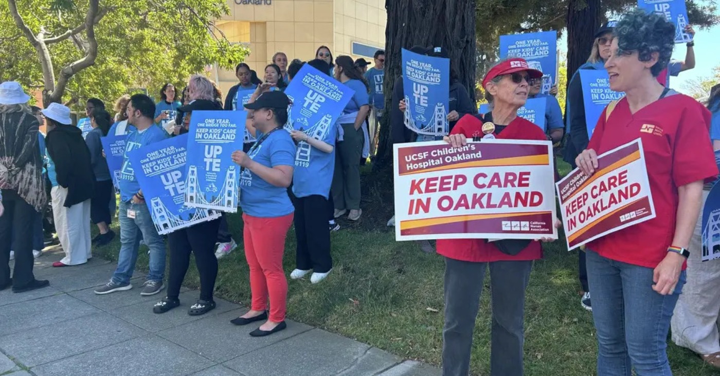 Staff and family members of patients at UCSF Benioff Children's Hospital Oakland in Oakland, Calif., hold signs during a rally on Thursday, July 9, 2026. Rally participants protested the relocation of specialized care clinics to the hospital's San Francisco campus. Photo by Kayla Chan/Bay City News.