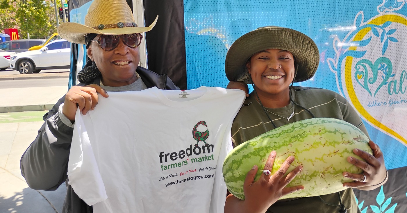 Elaine Smith, executive director of Farms to Grow, Inc., holds T-shirt for Ki’Ara LaFitte, winner of the Freedom Farmers’ Market Watermelon-Eating Contest at the season opening on July 11. Courtesy photo.